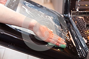 Housework and housekeeping concept. Scrubbing the stove and oven. Close up of female hand with green sponge cleaning the glass doo