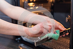 Housework and housekeeping concept. Scrubbing the stove and oven. Close up of female hand with green sponge cleaning the kitchen .