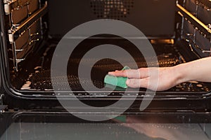 Housework and housekeeping concept. Scrubbing the stove and oven. Close up of female hand with green sponge cleaning the kitchen o