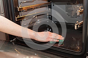 Housework and housekeeping concept. Scrubbing the stove and oven. Female hand with green sponge cleaning the kitchen oven..