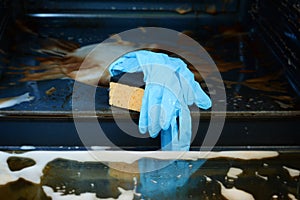 Housework and housekeeping concept. Scrubbing the stove and oven. Yellow sponge with soapy water and blue rubber gloves