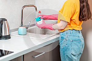 Housework. A housewife in casual clothes and pink rubber gloves is washing a cup. Side view