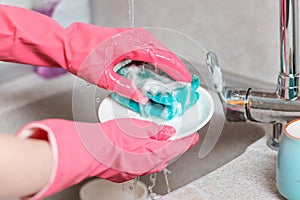 Housework. A woman in pink rubber gloves is washing dishes. Close up of kitchen sink and hands