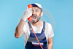 Housing maintenance call centre. Crazy handyman in overalls, safety gloves, shouting into retro phone handset