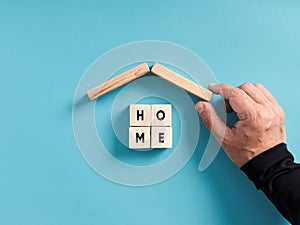 Housing, sheltering, home safety and security concept. Male hand building a house with wooden blocks with the word home