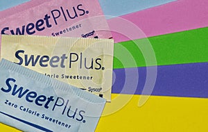 Sweet Plus artificial sweetener packets on colorful striped background.