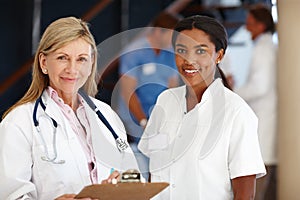 How can we help you. Portrait of two smiling female medical professionals.