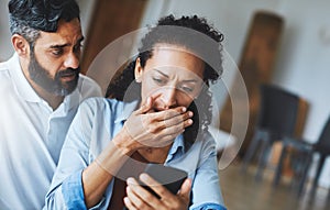 How could this happen. a dismayed couple receiving bad news via a smartphone at home. photo