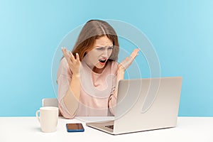How could you? Irritated young woman employee raising hands in indignant gesture, asking why and looking at laptop screen