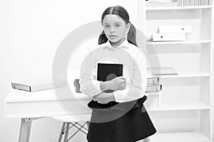 How make education more interesting for first formers. Girl child hold book while stand table white interior. Kid school