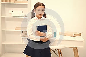 How make education more interesting for first formers. Girl child hold book while stand table white interior. Kid school