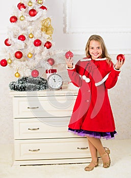 How to decorate christmas tree with kid. Girl smiling face hold balls ornaments white interior background. Let kid