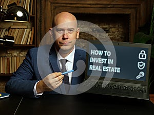 HOW TO INVEST IN REAL ESTATE phrase on the screen. Broker use internet technologies at office. Concept search and HOW TO INVEST