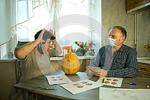 How to make Jack O`Lantern at home? A middle aged man and woman are doing Jack O`Lantern in the kitchen. There are masks on peop