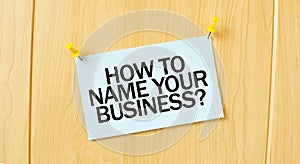 HOW TO NAME YOUR BUISINESS sign written on sticky note pinned on wooden wall photo