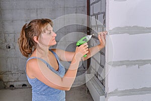 How to repair a new apartment yourself A young woman builder twists a screw into the wall with a screwdriver. Repair of the