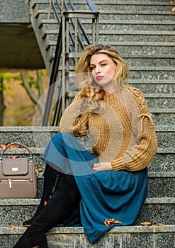 How to Style Sweater and Skirt Combo for Fall. Woman with gorgeous hairstyle sit on stairs outdoors. Fall fashion trend