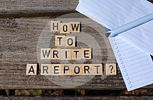 How to write a report? Black capital letter words on wooden toy blocks on a natural garden table background with paper and pencil.