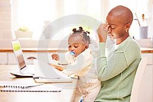 How will I get through this day. a young mother looking stressed while holding her baby and working from home.