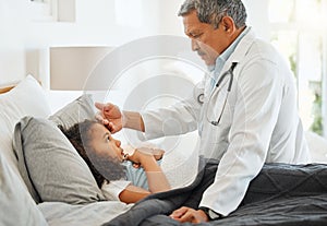 How are you feeling. a mature doctor checking a sick little girls temperature at home.