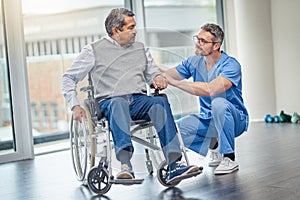 How are you finding your new wheelchair. a nurse helping a senior man in a wheelchair.