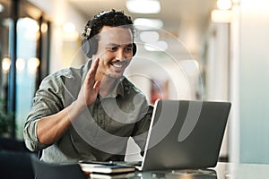Hows everyone doing today. a young businessman sitting in the office and wearing headphones while using his laptop for a