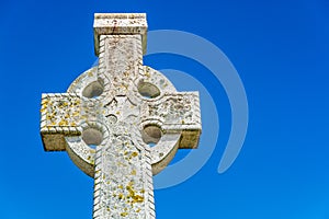 Old stone celtic cross on a bright clear blue sky background with empty copy space for text