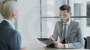 HR male manager having job interview with young woman in suit and watching her resume application in modern office