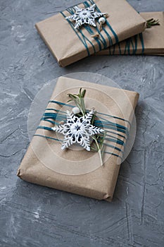 Hree Christmas gifts in craft paper wrapped in blue thread, with white snowflakes and rosemary branches on a gray concrete