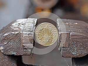 hryvnya coin clamped in a metal vise. Currency and Ukrainian economy under the onslaught