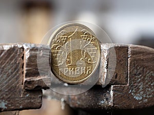 hryvnya coin clamped in a metal vise. Currency and Ukrainian economy under the onslaught, the concept of financial problems