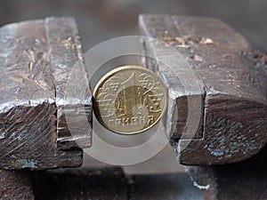 Hryvnya coin clamped in a metal vise. Currency and Ukrainian economy under the onslaught, the concept of financial problems