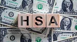 HSA symbol. Wooden cubes with the word `HSA - Health Savings Account`. Beautiful background from dollar bills. Business and HSA