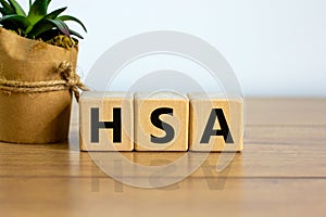 HSA symbol. Wooden cubes with word `HSA - Health Savings Account`. Beautiful wooden table, house plant. White background. Busine