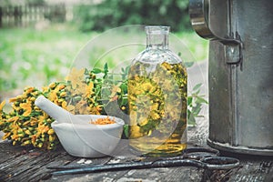 HSt Johns wort plants, oil or infusion transparent bottle, mortar on wooden table outdoors.