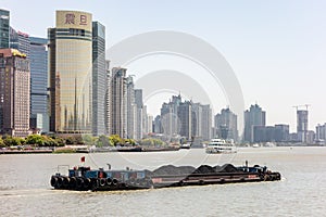 The Huangpu river in Shanghai, China with a cargo ship transfering goods. Modern scyscrapers of the Bund are in the background