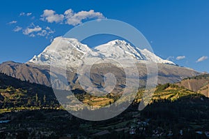 Huascaran mountain in Peru with its two snowy peaks rising over green valley where the town of Yungay sits,