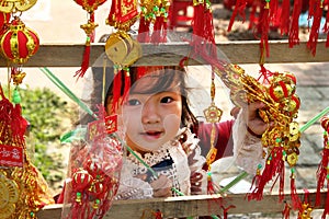 Portrait of little Vietnamese girl in red dress with traditional Vietnamese New Year decorations on the street of city.