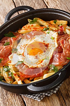 Huevos rotos con jamon fried egg with fries and ham close-up in a pan. vertical photo