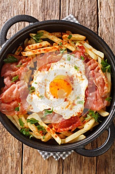 Huevos rotos con jamon fried egg with fries and ham close-up in a pan. vertical top view photo