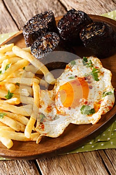 Huevos rotos con morcilla fried egg with fries and blood sausage close-up in a plate. vertical photo