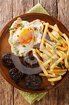 Huevos rotos con morcilla fried egg with fries and blood sausage close-up in a plate. vertical top view photo