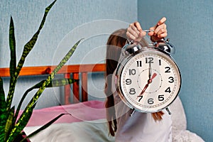 Huge alarm clock in the hands of a child in the bedroom. 7 o'clock in the morning on the clock.