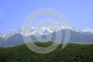 Huge alpine snow-covered ridge with Talgar peak with mountain ranges and green hills at the foot in summer, sunny