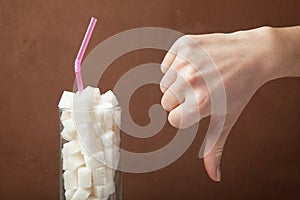 A huge amount of sugar in juice or soda drinks. Sugar cubes in glass and hand shows thumbs down