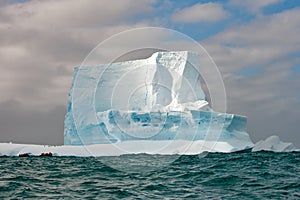 Huge antarctic table iceberg with penguins and tiny zodiac in front. Small boat with people in front of iceberg watching penguins.