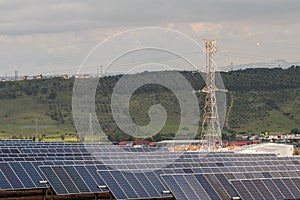 Huge area with a Transmission tower and large solar panels with green hills behind