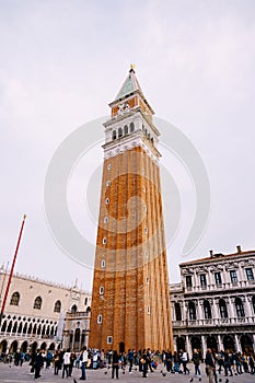 Huge bell tower made of red brick in Piazza San Marco - Campanile of St. Mark`s Cathedral in Venice, Italy. A crowd of