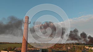 Huge black smoke from a fire in abandoned place with big red brick tube