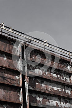 Huge bolted steel wall with pipes along the top, gray sky